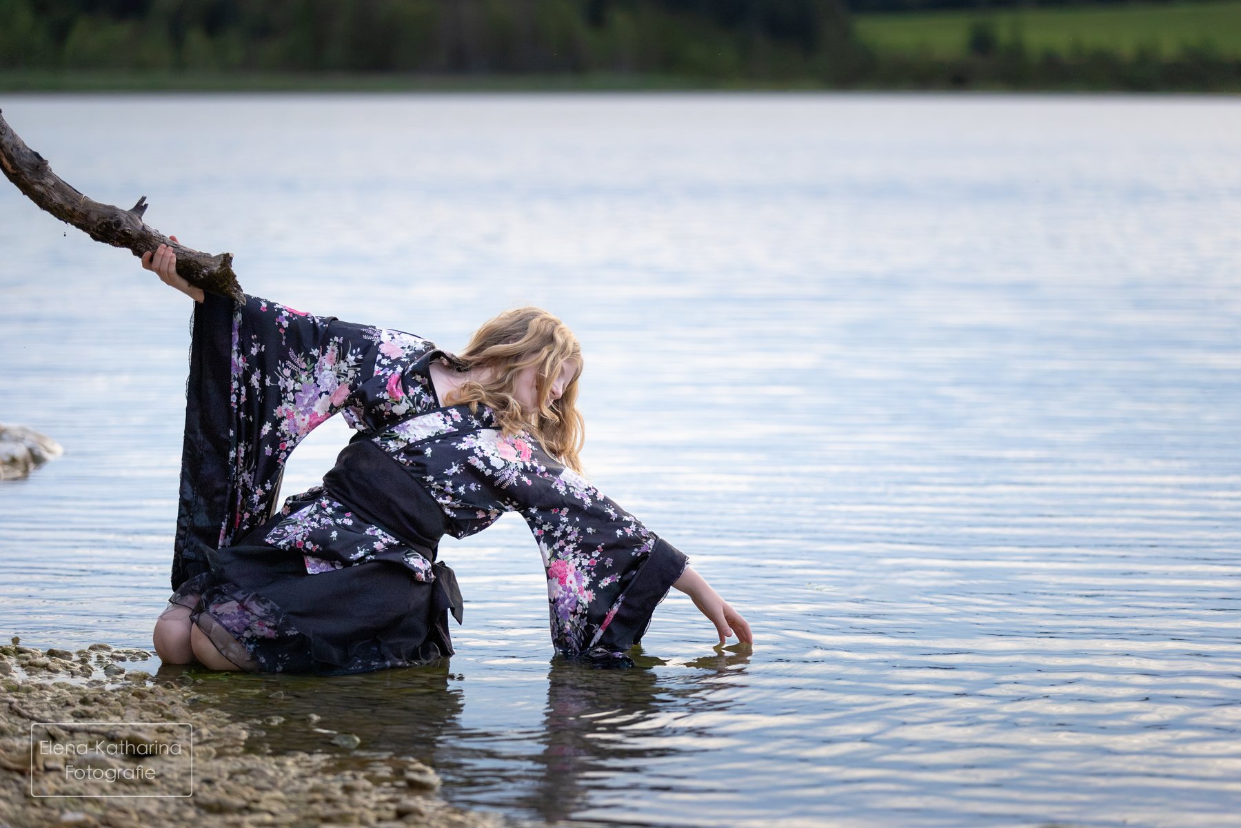 Junge Frau im kurzen Kimono hält sich an einem Ast und berührt das Wasser